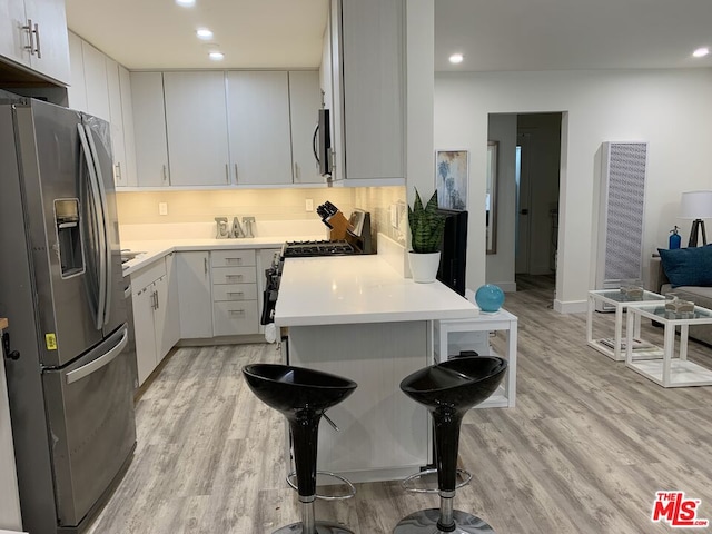 kitchen with stainless steel appliances, white cabinetry, a breakfast bar area, and light wood-type flooring