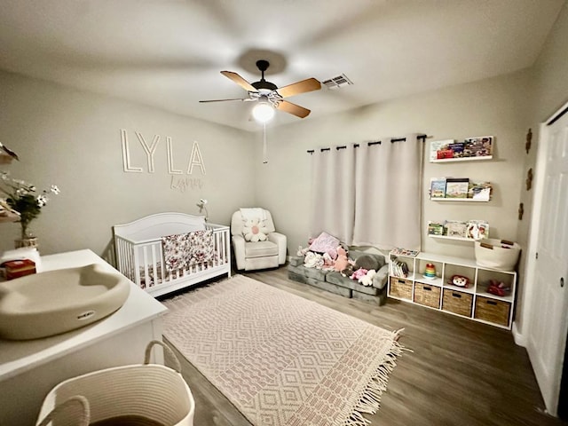 bedroom featuring a crib, dark hardwood / wood-style floors, and ceiling fan