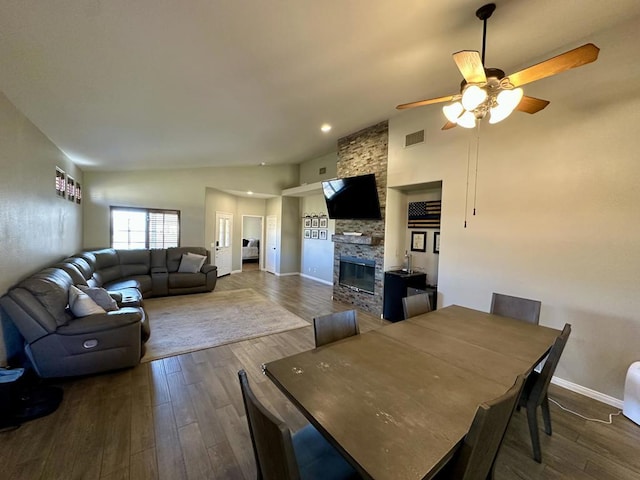 dining space with dark hardwood / wood-style flooring, a stone fireplace, high vaulted ceiling, and ceiling fan