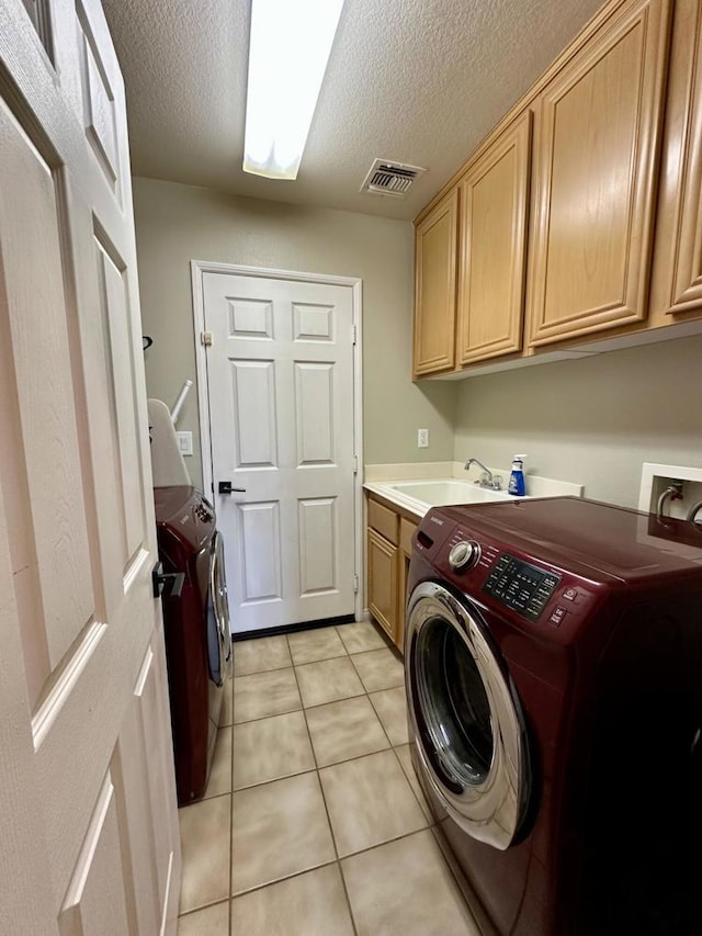 clothes washing area with light tile patterned flooring, cabinets, sink, and a textured ceiling