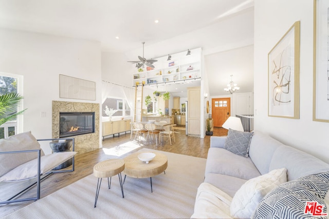 living room with hardwood / wood-style flooring, a premium fireplace, ceiling fan with notable chandelier, and high vaulted ceiling