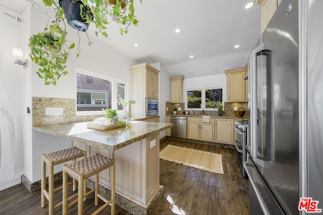 kitchen with a breakfast bar area, vaulted ceiling, appliances with stainless steel finishes, dark hardwood / wood-style flooring, and kitchen peninsula