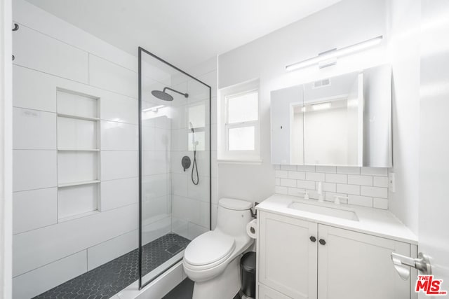 bathroom with vanity, decorative backsplash, toilet, and a tile shower