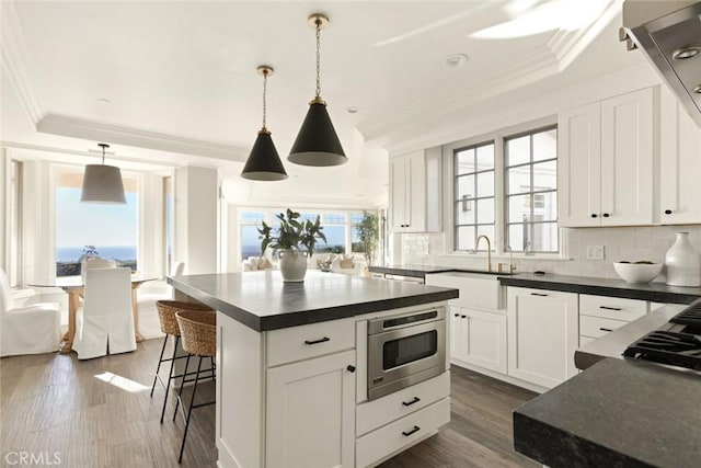 kitchen with stainless steel microwave, a kitchen island, pendant lighting, and white cabinets