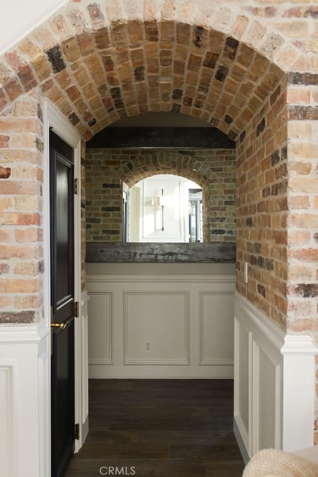 hall with dark hardwood / wood-style flooring, brick ceiling, and brick wall