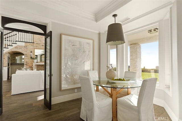 dining space with brick wall, ornamental molding, dark hardwood / wood-style floors, and a tray ceiling