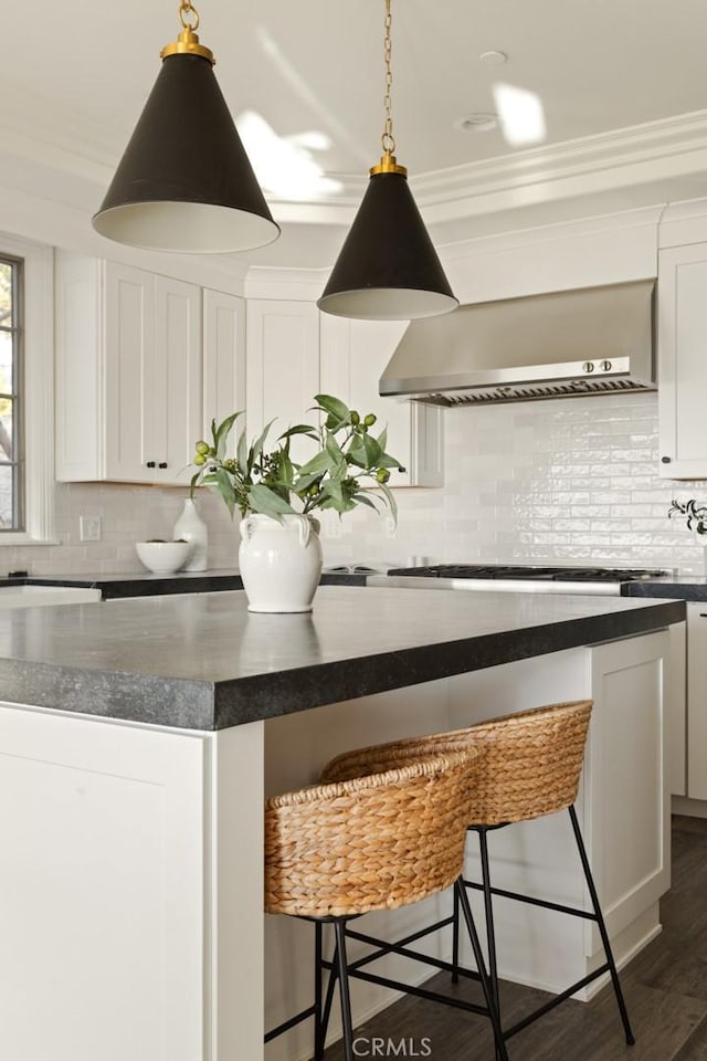 kitchen featuring backsplash, white cabinets, a kitchen breakfast bar, dark wood-type flooring, and wall chimney range hood