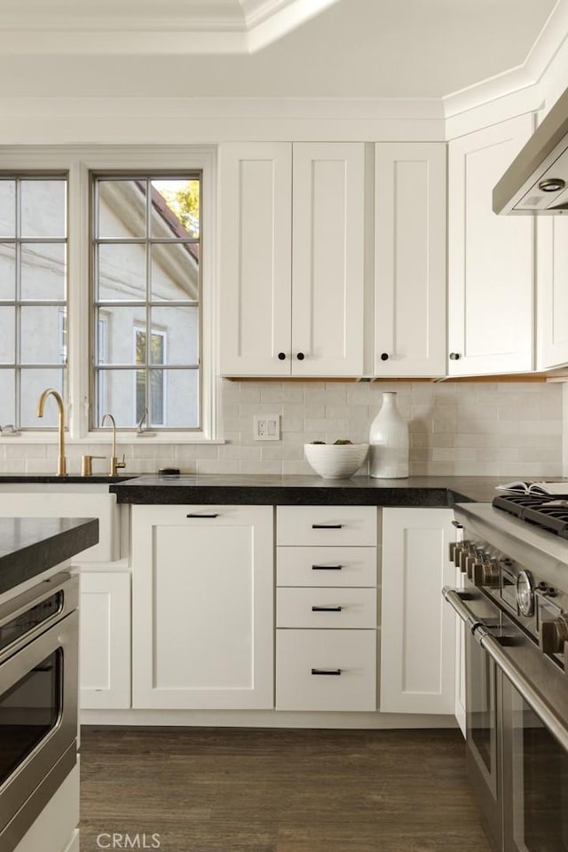 kitchen with dark hardwood / wood-style floors, white cabinets, stainless steel appliances, decorative backsplash, and wall chimney range hood