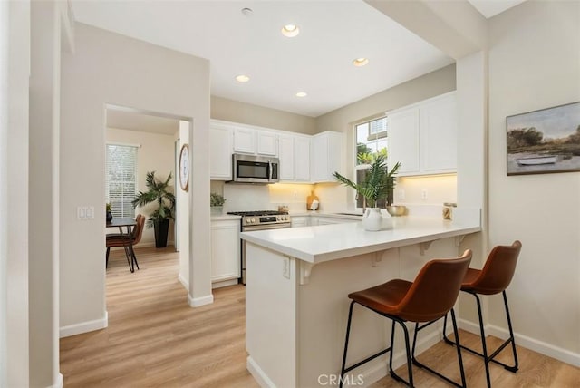 kitchen featuring appliances with stainless steel finishes, white cabinetry, a breakfast bar area, kitchen peninsula, and light wood-type flooring