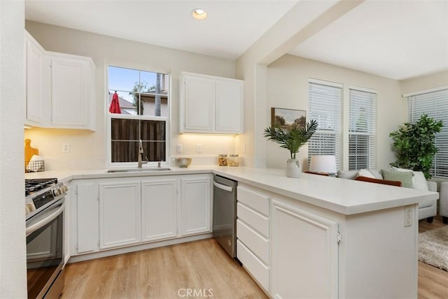 kitchen with sink, light hardwood / wood-style flooring, white cabinetry, stainless steel appliances, and kitchen peninsula