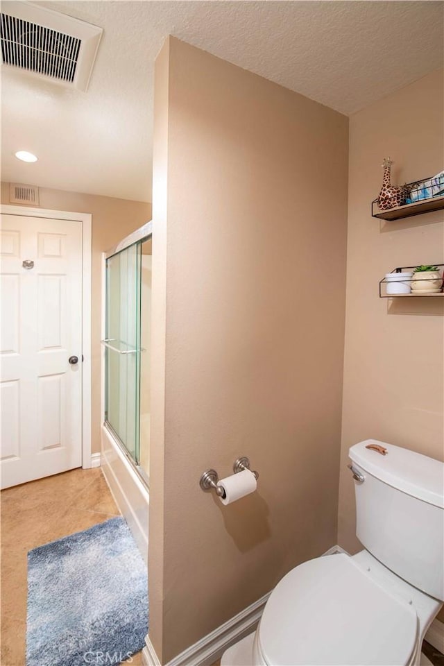 bathroom with combined bath / shower with glass door, a textured ceiling, and toilet