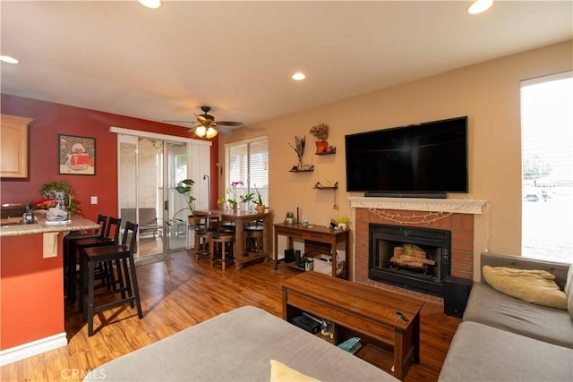 living room with a fireplace, wood-type flooring, sink, and ceiling fan