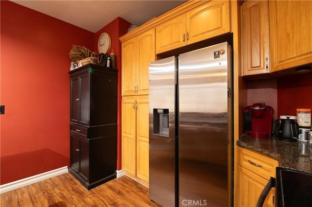 kitchen with dark stone countertops, stainless steel fridge, stove, and light hardwood / wood-style flooring