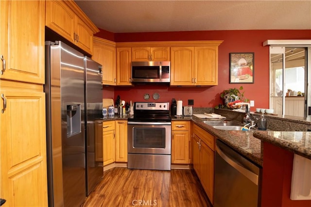 kitchen featuring stainless steel appliances, sink, hardwood / wood-style floors, and dark stone counters