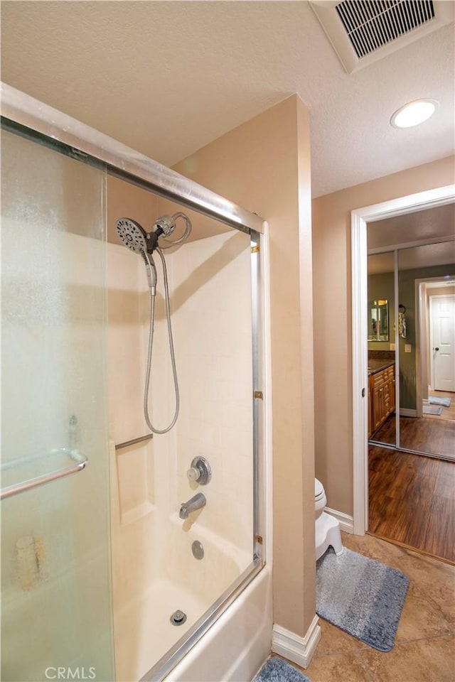 bathroom featuring toilet, bath / shower combo with glass door, and a textured ceiling