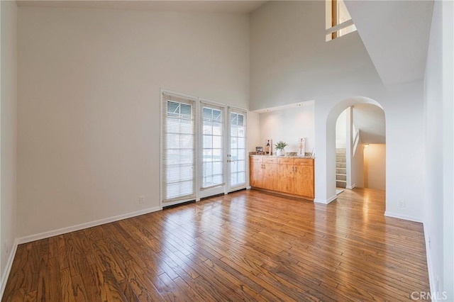 empty room featuring a towering ceiling, baseboards, arched walkways, and wood finished floors