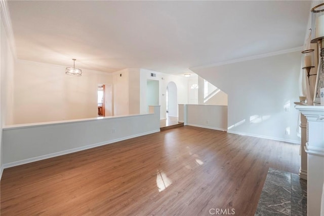 unfurnished living room with baseboards, arched walkways, wood finished floors, and ornamental molding