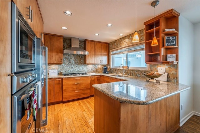 kitchen with stainless steel appliances, brown cabinets, a sink, and wall chimney range hood