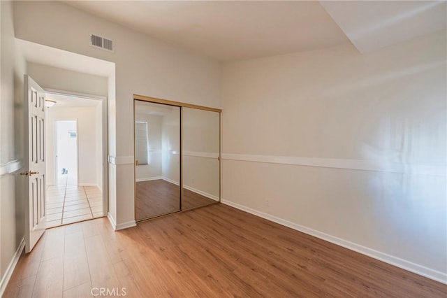 unfurnished bedroom featuring baseboards, a closet, visible vents, and wood finished floors