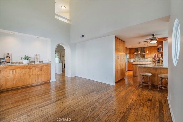 living area with arched walkways, visible vents, ceiling fan, wood finished floors, and baseboards