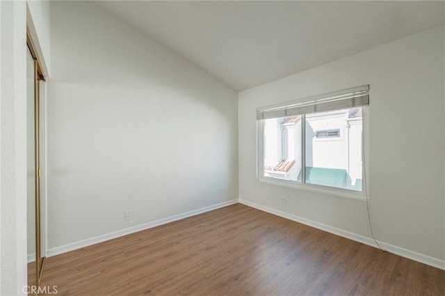 unfurnished room with baseboards, vaulted ceiling, and wood finished floors