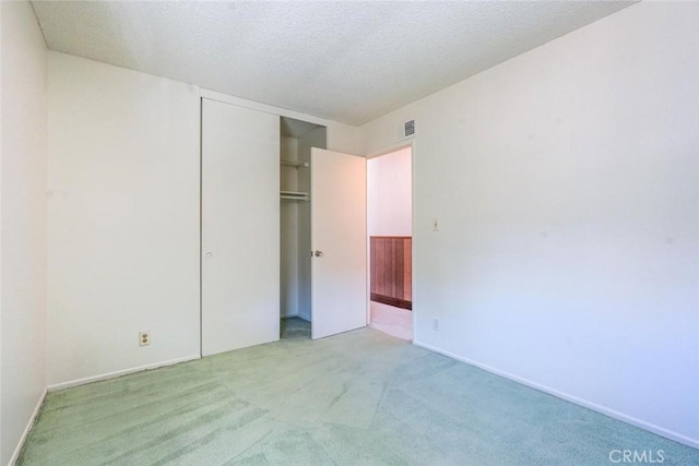 unfurnished bedroom with light colored carpet, a closet, and a textured ceiling