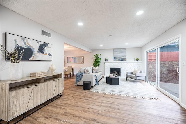 living room with a stone fireplace, a textured ceiling, and light hardwood / wood-style flooring