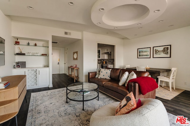 living room with dark wood-type flooring and a tray ceiling