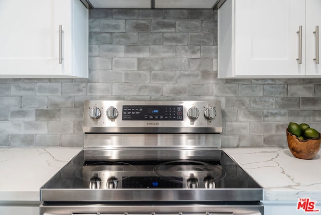 kitchen featuring electric range, light stone countertops, and white cabinets