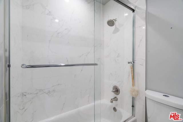 bathroom with combined bath / shower with glass door and toilet