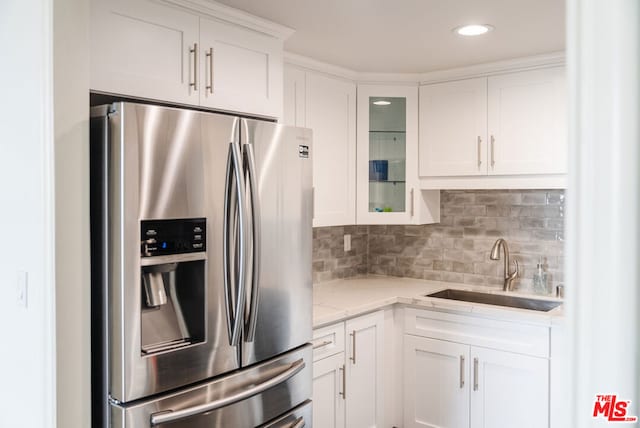 kitchen with sink, light stone counters, stainless steel fridge with ice dispenser, decorative backsplash, and white cabinets