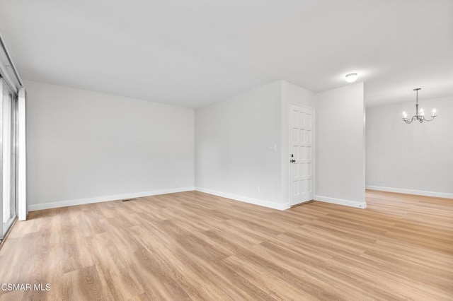 spare room featuring an inviting chandelier and light hardwood / wood-style floors