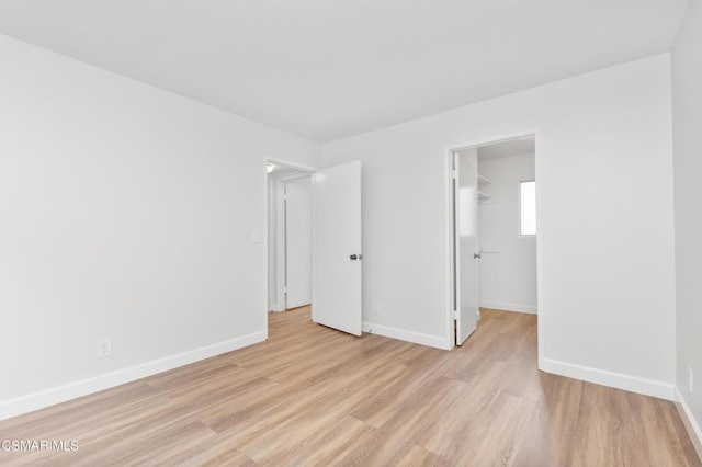 unfurnished bedroom with a spacious closet, a closet, and light wood-type flooring