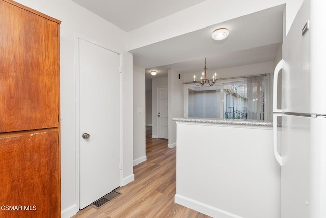 kitchen with white fridge, a notable chandelier, pendant lighting, light stone countertops, and light hardwood / wood-style floors