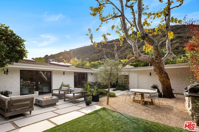 back of property with a mountain view, a patio area, and an outdoor living space with a fire pit