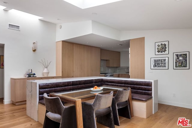 dining area with vaulted ceiling with skylight and light wood-type flooring