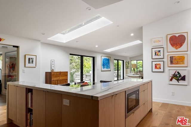 kitchen with a skylight, black microwave, a kitchen island, and light hardwood / wood-style flooring