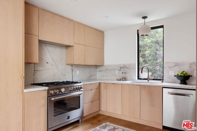 kitchen with stainless steel appliances, hanging light fixtures, sink, and light brown cabinetry