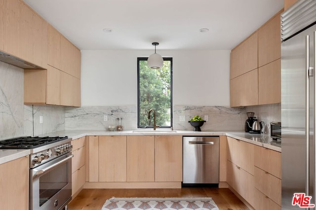 kitchen featuring decorative light fixtures, high quality appliances, sink, light brown cabinets, and light hardwood / wood-style flooring