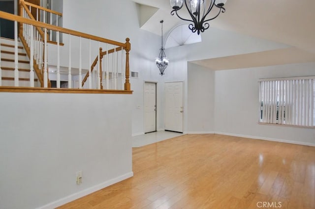 unfurnished living room with an inviting chandelier, high vaulted ceiling, and hardwood / wood-style flooring