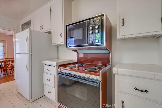 kitchen featuring white refrigerator, range with electric stovetop, tile countertops, and white cabinets