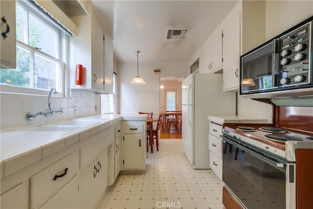 kitchen featuring tile countertops, sink, white cabinets, hanging light fixtures, and white appliances