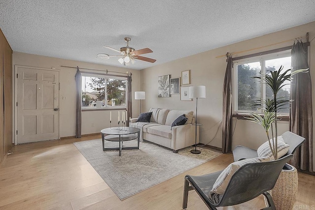 living room with a textured ceiling, ceiling fan, and light wood-type flooring