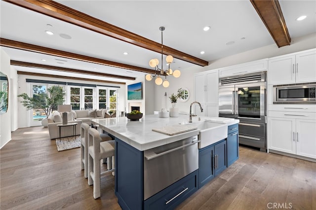 kitchen with built in appliances, hanging light fixtures, white cabinetry, and an island with sink