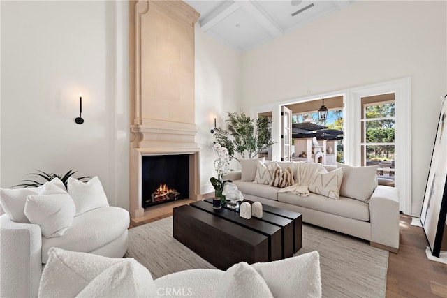 living room featuring coffered ceiling, light hardwood / wood-style flooring, a large fireplace, beam ceiling, and a high ceiling