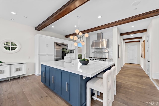 kitchen with a kitchen island, built in appliances, blue cabinets, decorative light fixtures, and wall chimney exhaust hood