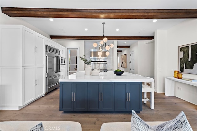 kitchen with decorative light fixtures, blue cabinets, white cabinetry, built in appliances, and beam ceiling