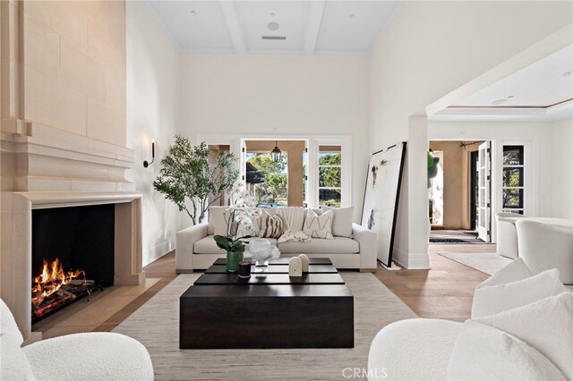 living room featuring a towering ceiling, beamed ceiling, and light wood-type flooring