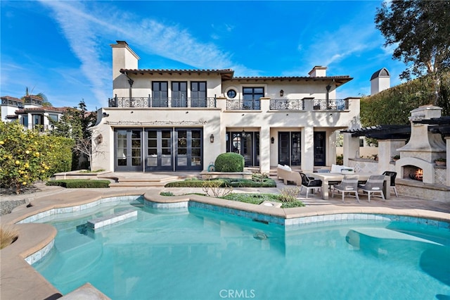 rear view of property with a balcony, a patio, and an outdoor fireplace