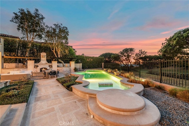 pool at dusk featuring an outdoor fireplace and a patio area